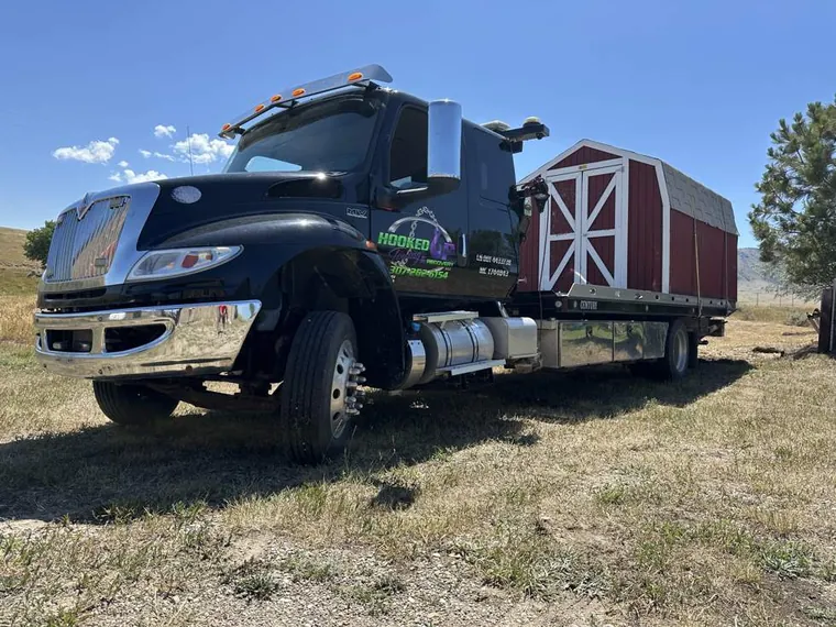 Red barn shed being moved on Hooked Up Towing flatbed truck in Wyoming