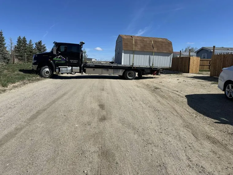 White storage shed transported on flatbed by Hooked Up Towing and Recovery